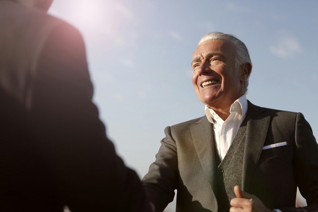 pexels-photo-3781915-3781915 Elderly man in formal wear smiling while shaking hands outside during the day.