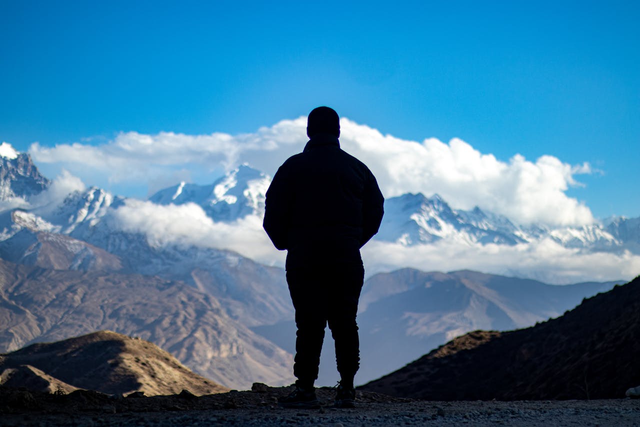 Man silhouetted against a breathtaking mountain landscape with clear skies and majestic snow-capped peaks.